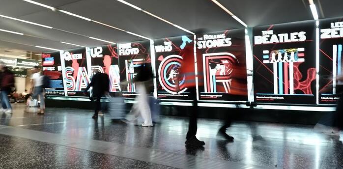 Visitors walking past illuminated Rock Icons displays at Milan Malpensa Airport