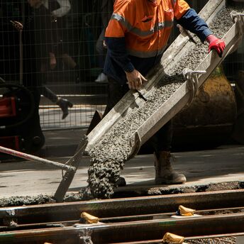 Construction worker pouring concrete beside railway tracks