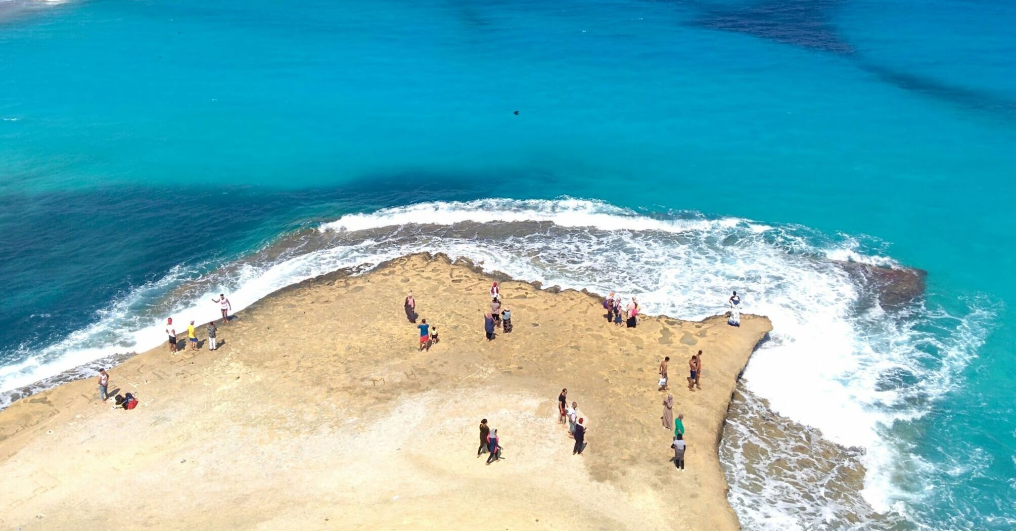 People standing on a rocky outcrop surrounded by turquoise sea