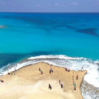People standing on a rocky outcrop surrounded by turquoise sea