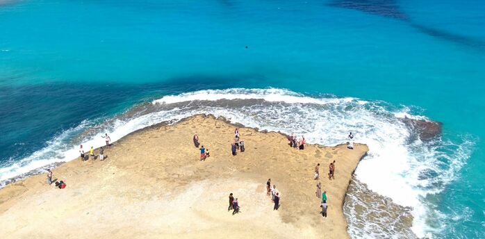 People standing on a rocky outcrop surrounded by turquoise sea