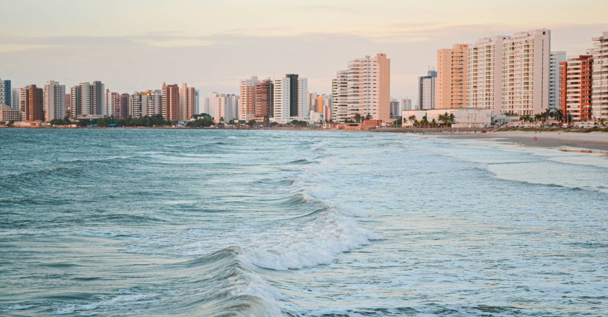 Ocean waves rolling towards a sandy beach with high-rise buildings along the coast