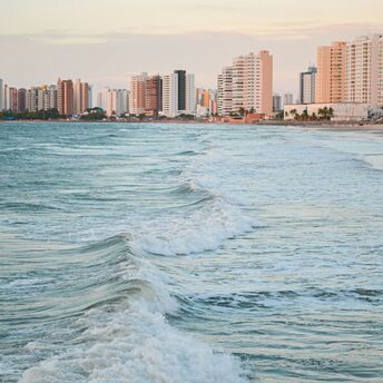Ocean waves rolling towards a sandy beach with high-rise buildings along the coast