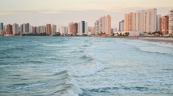 Ocean waves rolling towards a sandy beach with high-rise buildings along the coast