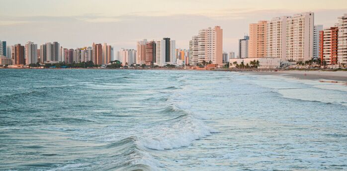 Ocean waves rolling towards a sandy beach with high-rise buildings along the coast
