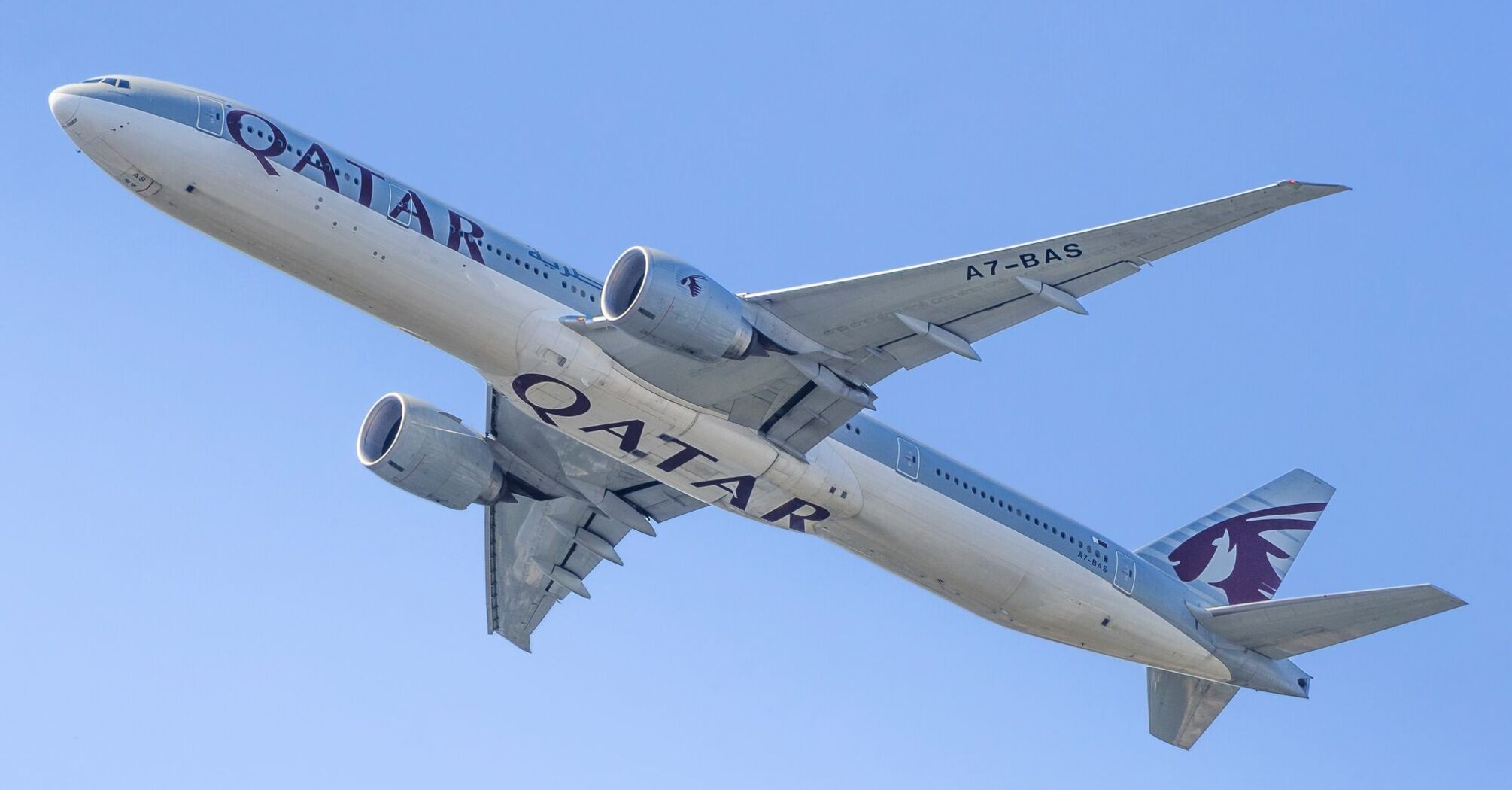 Qatar Airways passenger aircraft flying against a clear blue sky, viewed from below