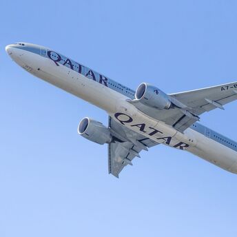Qatar Airways passenger aircraft flying against a clear blue sky, viewed from below