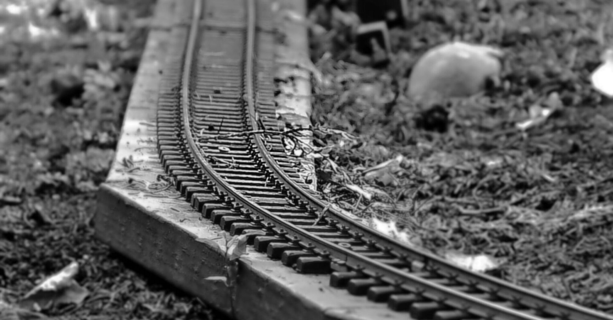 Black and white close-up of a damaged miniature railway track with bent rails and scattered debris