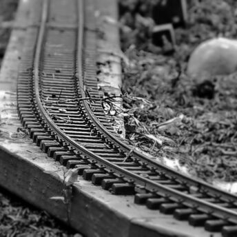 Black and white close-up of a damaged miniature railway track with bent rails and scattered debris