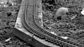 Black and white close-up of a damaged miniature railway track with bent rails and scattered debris
