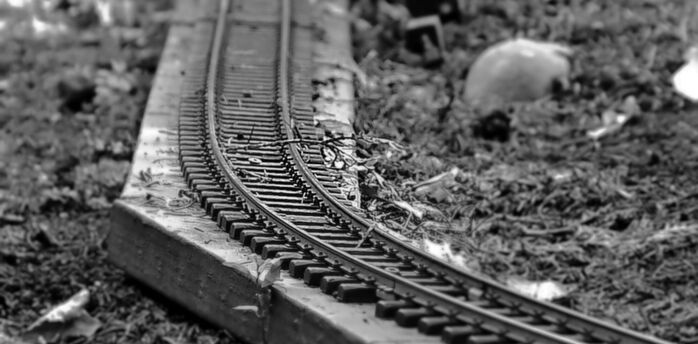 Black and white close-up of a damaged miniature railway track with bent rails and scattered debris