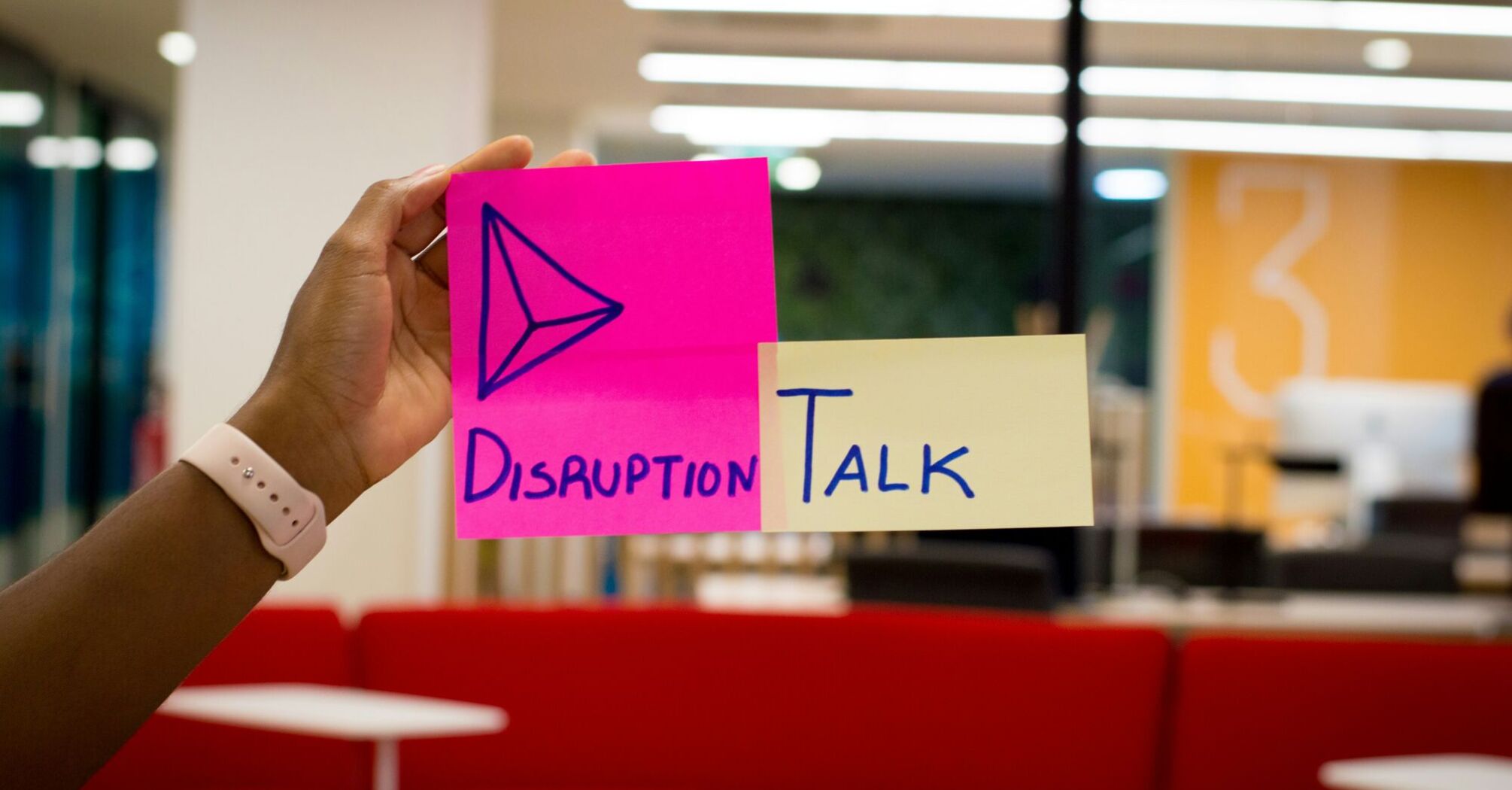 Hand holding colourful sticky notes with the words "Disruption Talk" in an office