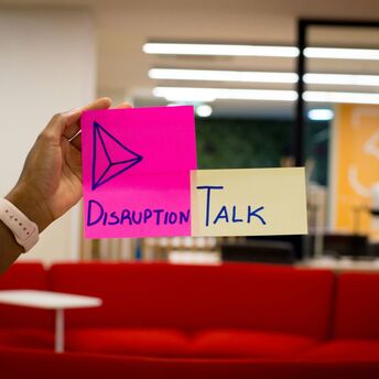 Hand holding colourful sticky notes with the words "Disruption Talk" in an office