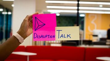 Hand holding colourful sticky notes with the words "Disruption Talk" in an office