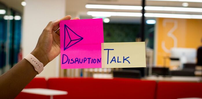 Hand holding colourful sticky notes with the words "Disruption Talk" in an office