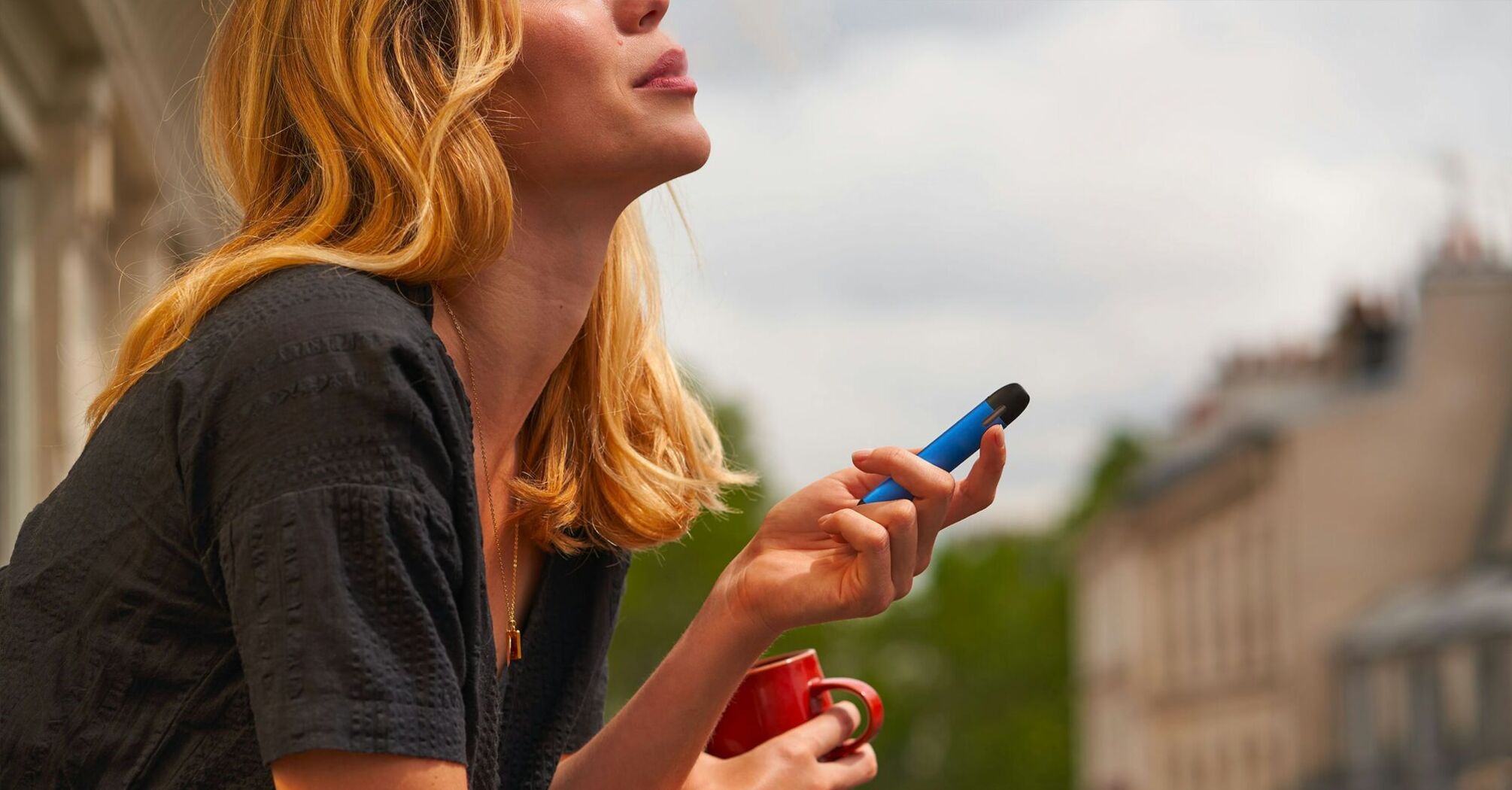Woman holding a blue vape and a red cup outdoors
