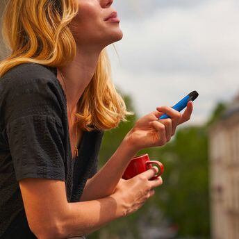 Woman holding a blue vape and a red cup outdoors