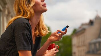 Woman holding a blue vape and a red cup outdoors