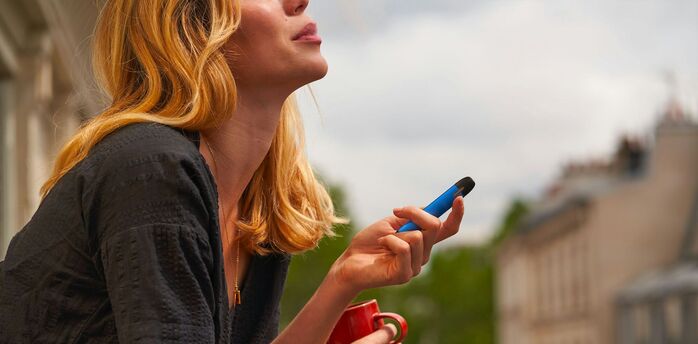 Woman holding a blue vape and a red cup outdoors