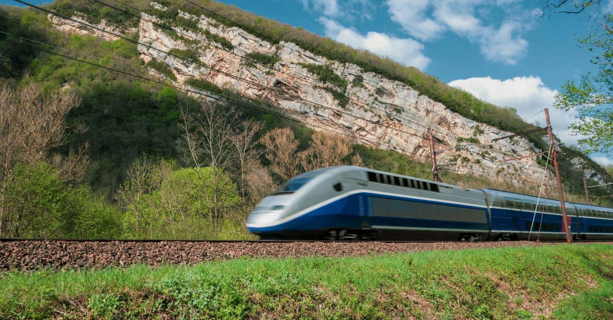 High-speed passenger train travelling past wooded cliffs