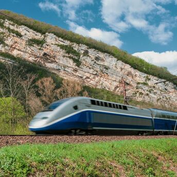 High-speed passenger train travelling past wooded cliffs