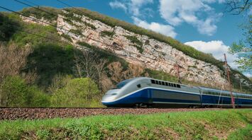 High-speed passenger train travelling past wooded cliffs