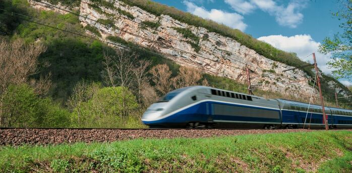 High-speed passenger train travelling past wooded cliffs