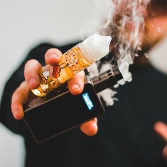 Person holding a vape and e-liquid bottle