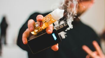 Person holding a vape and e-liquid bottle