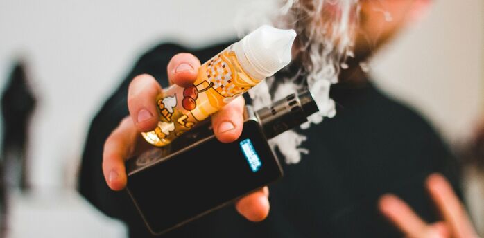 Person holding a vape and e-liquid bottle
