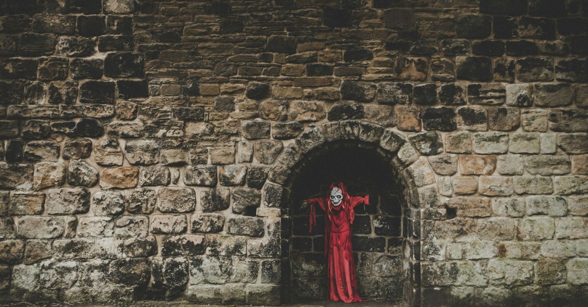Red-cloaked Halloween figure standing in a dark stone archway