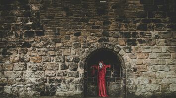 Red-cloaked Halloween figure standing in a dark stone archway