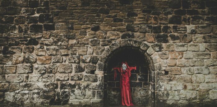 Red-cloaked Halloween figure standing in a dark stone archway