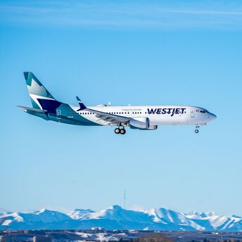 WestJet aircraft flying above snow-covered mountains
