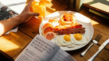 Plate of eggs, bacon and pancakes with orange juice on a breakfast table