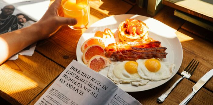 Plate of eggs, bacon and pancakes with orange juice on a breakfast table