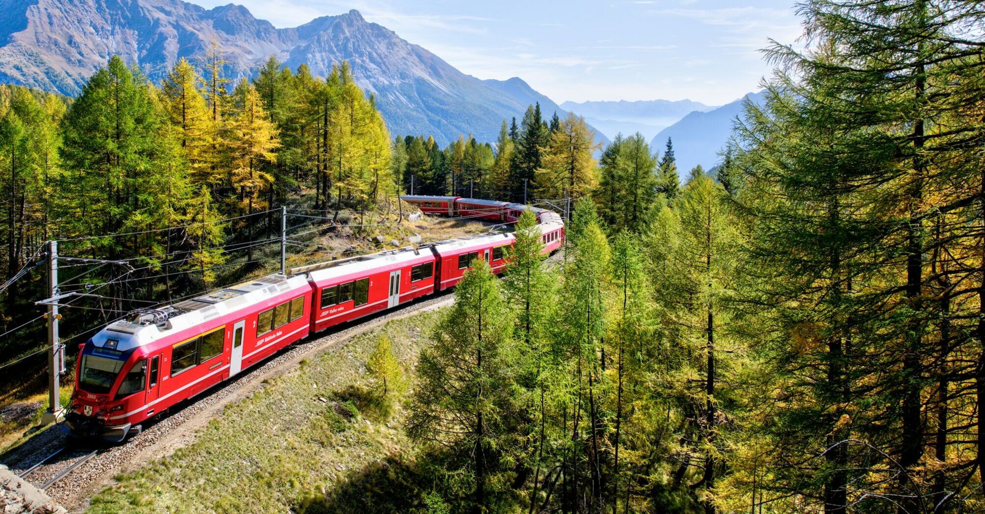 Red train travelling through an Alpine landscape