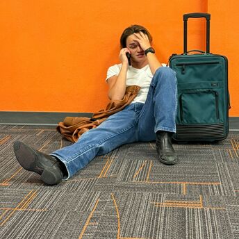 Stranded traveller sitting at airport with suitcase after flight cancellation
