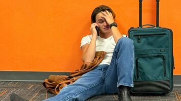Stranded traveller sitting at airport with suitcase after flight cancellation