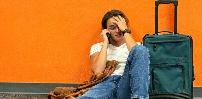 Stranded traveller sitting at airport with suitcase after flight cancellation