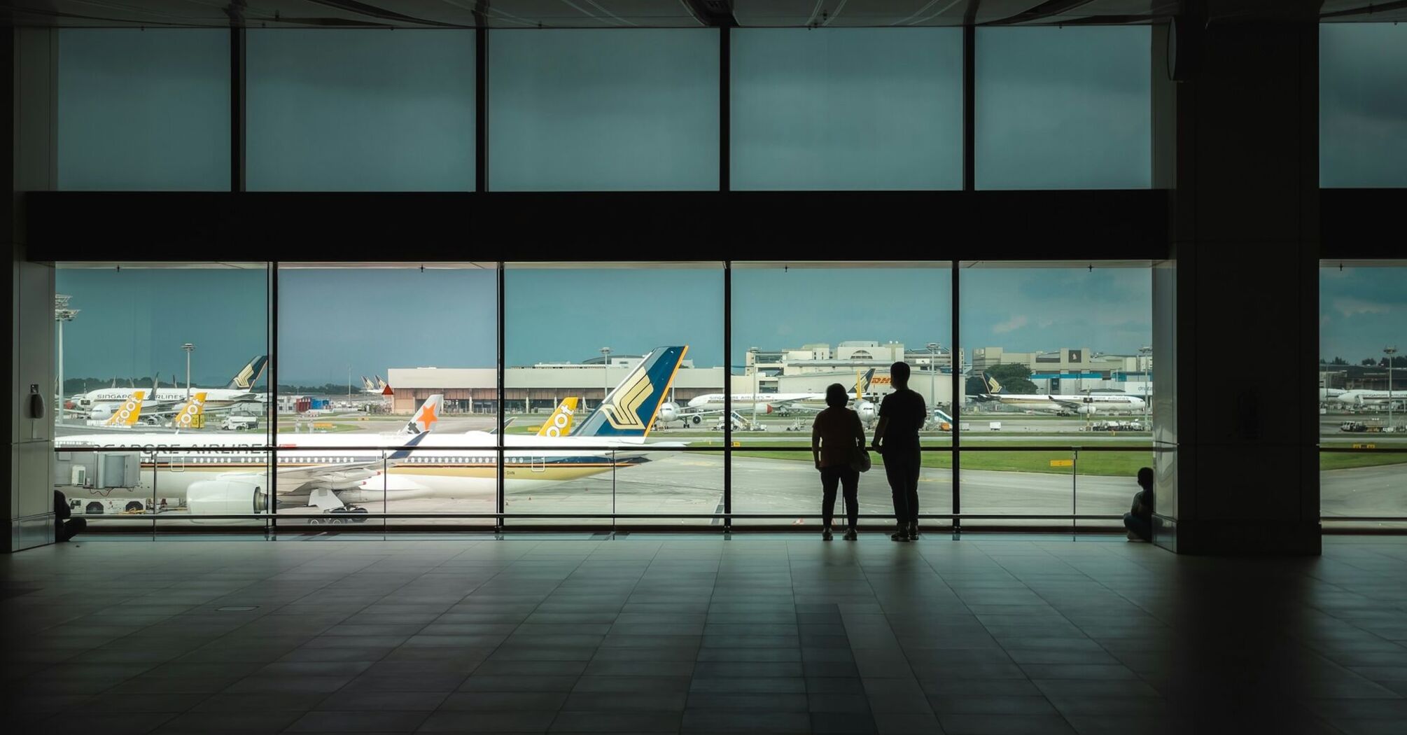 Passengers waiting inside airport terminal overlooking runway