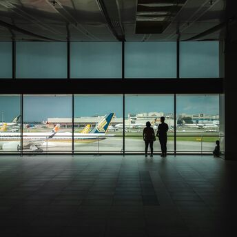 Passengers waiting inside airport terminal overlooking runway