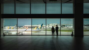Passengers waiting inside airport terminal overlooking runway