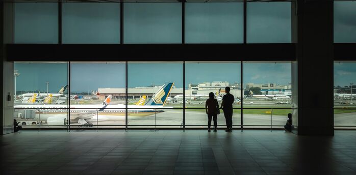 Passengers waiting inside airport terminal overlooking runway