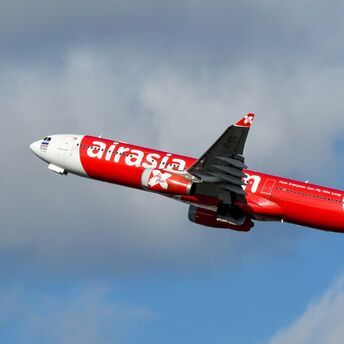 AirAsia X Airbus aircraft in red livery climbing after take-off against a cloudy sky