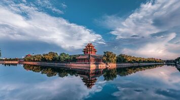 Corner tower of the Forbidden City reflected in water at sunset