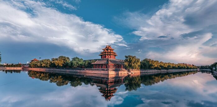 Corner tower of the Forbidden City reflected in water at sunset