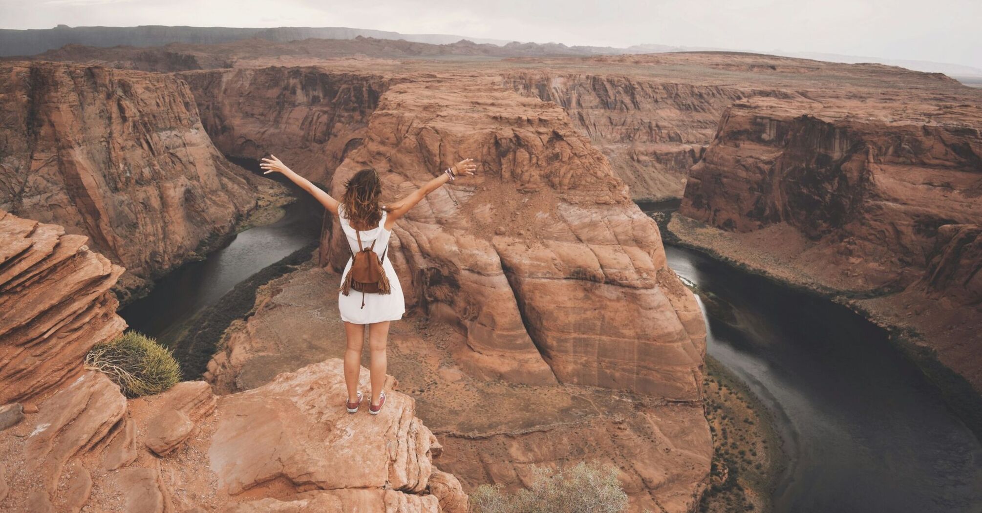 Traveller standing on canyon cliff overlooking winding river in the US Southwest