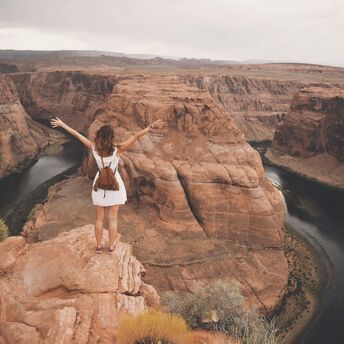 Traveller standing on canyon cliff overlooking winding river in the US Southwest
