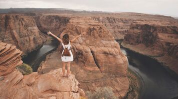 Traveller standing on canyon cliff overlooking winding river in the US Southwest